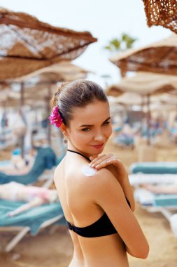 Bikinili güzel genç kadın güneş altında sahilde cilt üzerinde koruyucu krem yayma. Güneş kremi şişe onun elinde tutan seksi genç kadın bikini. Cilt Bakımı.
