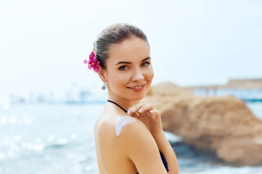 Kadına uygulanan güneş koruyucu krem tabaklanmış omuz gülümse. Cilt Bakımı. Güneş koruma güneş kremi vücut. Nemlendirici losyon geri Bikini kadın smear.
