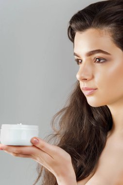 Cilt Bakımı. Güzellik kavramı. Kozmetik krem tutan genç güzel kadın. Yumuşak deri ve çıplak omuz, model makyajlı ışık çıplak, kadın tutarak onun elinde krem nemlendirici portresi. Cilt koruma ve Dermatoloji.