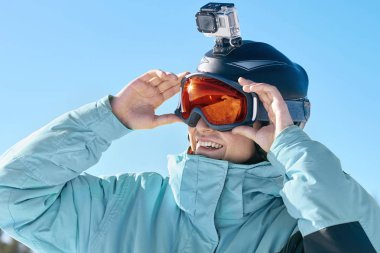 Kayakçı ile eylem fotoğraf makinesi üzerinde bir kask. Kayak kar yağdı dağlara yansıması ile gözlükler. Adamın dağlar ve mavi gökyüzü arka plan üzerinde Kayak Merkezi, portre. Kayak gözlüklü