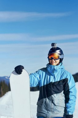 Kamera bir kask ile snowboard. Kayak kar yağdı dağlara yansıması ile gözlükler. Adam arka plan mavi gökyüzü üzerinde Kayak Merkezi, portresi snowboard tutun. Kayak gözlüklü
