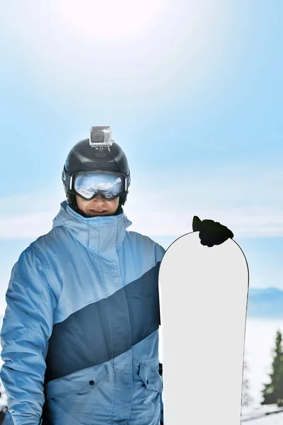ヘルメットにアクション カメラとスノーボーダー スキーは 雪が降った山の反射でゴーグルします 青色の背景の空のスキー場での男の肖像画は スノーボードを保持します スキー用メガネ — ストック写真