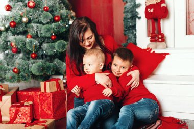 Mutlu genç anne ile iki çocuk tutan Noel hediyesi ve gülen, kamera yakın Noel ağacı. Yeni yıl kutlama. Aile bir Noel ağacı süsle