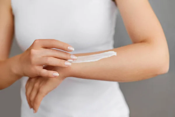 Closeup shot of woman hands holding cream and applying moisturizing hand cream. Beautiful female hands with cream. Hand Skin Care. A woman uses body lotion on your arms. Beauty And Body Care Concept