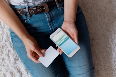 Kredi kartı tutan ve telefonunuzun ve katta oturan genç kadın. Ödeme. Online alışveriş kavramı. Bloglama kavramını. Modern teknolojiler Üstten Görünüm.