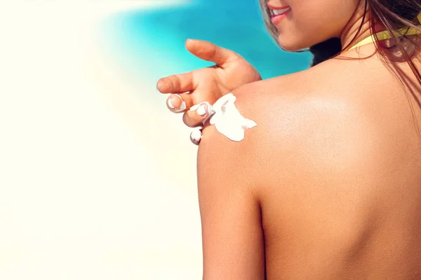 Woman putting sunblock lotion on shoulder before tanning during summer holiday on beach vacation resort