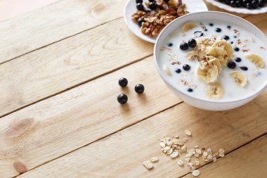 Muz, fındık, kuru üzüm, yaban mersini ve ahşap arka plan üzerinde masada süt ile yulaf ezmesi lapası. Sağlıklı kahvaltı ve diyet gıda. Üstte görüntü