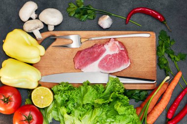 Koyu arka planda çiğ et sağlıklı yemek için taze malzemelerle çiğ organik sebzeler. Biberiye ve baharatlar ile kesme tahtası üzerinde çiğ sığır eti biftek. Üstte görüntü.