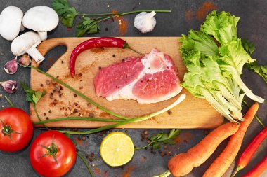Koyu arka planda çiğ et sağlıklı yemek için taze malzemelerle çiğ organik sebzeler. Biberiye ve baharatlar ile kesme tahtası üzerinde çiğ sığır eti biftek. Üstte görüntü.