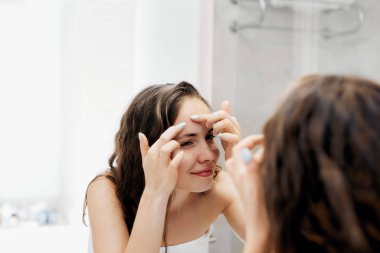 Genç bir kadın aynanın önünde sivilceli birine bakıyor ve onu sıkıyor. Çirkin sorunlu cilt kızı, sivilceli genç kız. Cilt bakımı. Güzellik