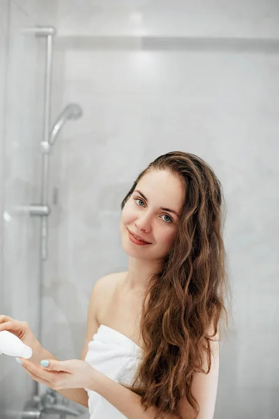 아름다운 여성은 화장실에서 서있는 머리와 미소로 로션을 적용합니다 모발과 피부를 — 스톡 사진