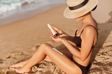 Güneş onun elinde şişe tutan bir kadın. Cilt Bakımı. Güneş koruma güneş krem düzgün tabaklanmış bacaklarını. Suncream ve tabaklanmış kadın ayak plaj üzerinde