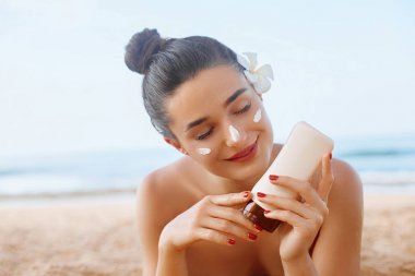Güzel Kadın gülümseme yüzünde güneş kremi uygulayarak. Cilt ve Vücut Bakımı. Güneş koruması. Bikinili kız sahilde güneş kremi şişesi tutuyor. Şapka lı kadın ciltte nemlendirici losyon