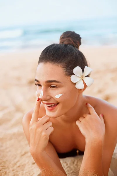 Skin care. Sun protection. Beautiful Woman In Bikini apply sun cream on Face. Woman With Suntan Lotion On Beach. Portrait Of Female Holding Moisturizing Sunblock.The Girl Uses Sunscreen for Her Skin.