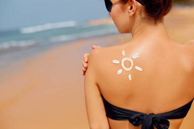 Kumsalda güneş krem şişe tutan omuz üzerinde güneş şekli olan kadın