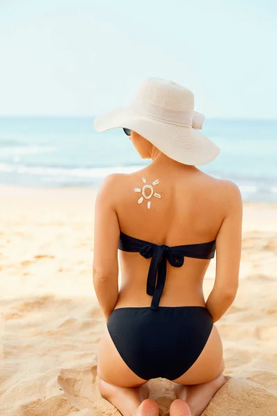 Woman Applying Sun Cream Creme on Tanned  Shoulder In Form Of The Sun. Sun Protection. Skin Care. Girl Using Sunscreen to Skin. Portrait Of Female Holding Suntan Lotion and Moisturizing Sunblock.