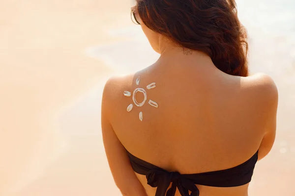 Sun cream. Suntan lotion beautiful woman applying on tanned shoulder in form of the sun. Sunscreen solar cream. Skin care. Sun protection.The Girl uses moisturizer sunblock