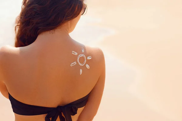 Sun cream. Suntan lotion beautiful woman applying on tanned shoulder in form of the sun. Sunscreen solar cream. Skin care. Sun protection.The Girl uses moisturizer sunblock