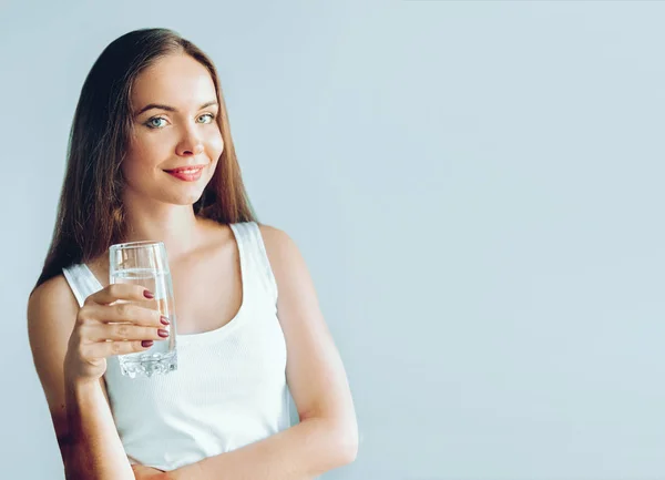 Healthy lifestyle. Young woman show glass of water. Girl drinks water. Portrait of happy smiling female model  holding transparent glass of water. Health,Beauty, Diet concept