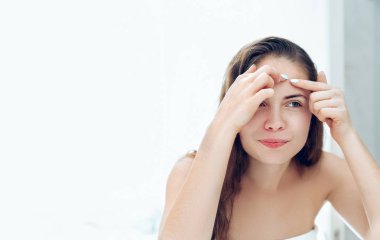 Genç bir kadın aynanın önünde sivilceli birine bakıyor ve onu sıkıyor. Çirkin sorunlu cilt kızı, sivilceli genç kız. Cilt bakımı. Güzellik