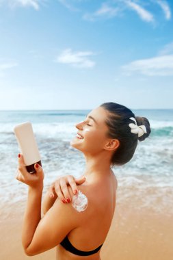 Bronzlaşmış omzuna güneş kremi süren bir kadın. Cilt bakımı. Güneş korumalı güneş kremi. Bikini şapkalı kadın sırtına nemlendirici güneş kremi sürüyor..