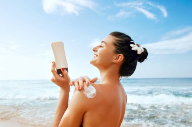 Bronzlaşmış omzuna güneş kremi süren bir kadın. Cilt bakımı. Güneş korumalı güneş kremi. Bikini şapkalı kadın sırtına nemlendirici güneş kremi sürüyor..
