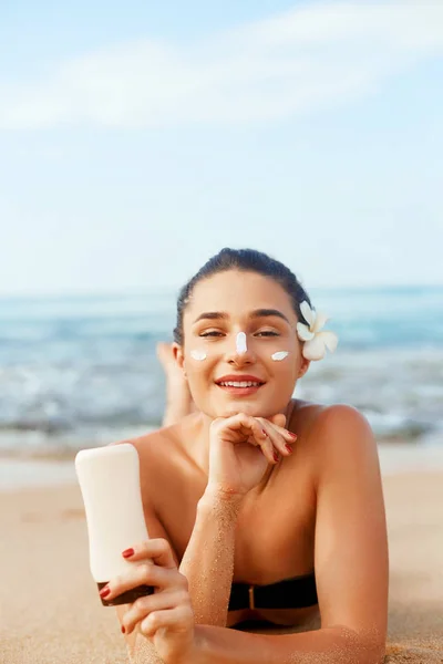 Sunscreen woman applying suntan lotion showing bottle. Beautiful smiling happy woman with suntan cream  lying on beach.  Skin care. Body Sun protection.Sun cream on face.