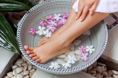 Spa tedavisi ve kadın ayak ve ayak spa için ürün. Tropikal çiçekler, Tayland ile kase ayak banyosu. Sağlıklı Konsept. Pedikür prosedürü nde spa salonunda güzel kadın ayakları, bacaklar Closeup.