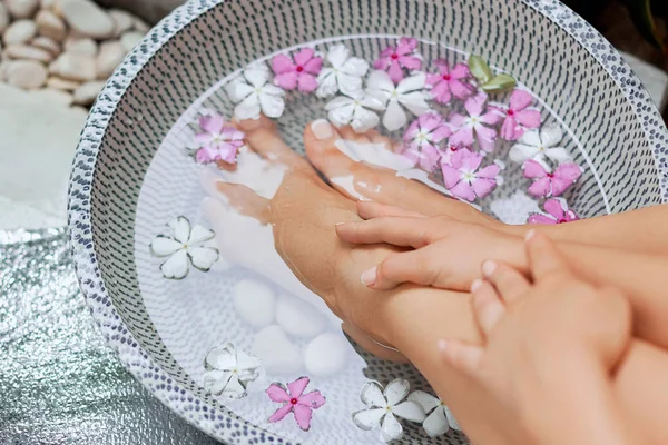 Spa treatment and product for woman feet and foot spa. Foot bath in bowl with tropical flowers, Thailand. Healthy Concept. Closeup  of  beautiful female feet, legs at spa salon on pedicure procedure