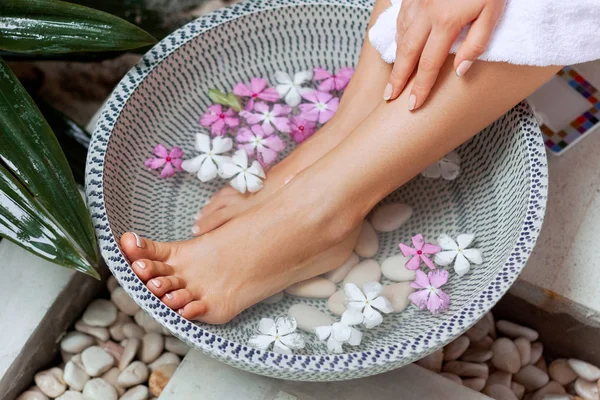 Spa treatment and product for woman feet and foot spa. Foot bath in bowl with tropical flowers, Thailand. Healthy Concept. Closeup  of  beautiful female feet, legs at spa salon on pedicure procedure.