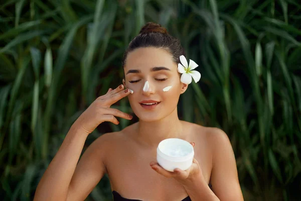 Beauty Woman Concept. Skin care.  Portrait of female model  holding and applying cosmetic moisturizing cream and touch own face. Nude make-up. Skin Protection