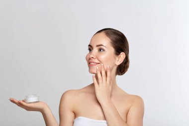 Skin care. Beauty Concept. Young woman holding cosmetic cream. Soft skin model with nude make-up. Portrait of female holding moisturizing cream and touch own face. Skin Protection and dermatology. clipart