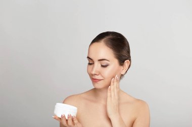 Güzellik Kadın Yüz Cilt Bakımı. Çekici Genç Kadın Uygulama Krem ve Holding Şişe Portresi. Doğal Makyaj ve Taze Cilt ile Gülümseyen Kız Closeup. Güzellik Kozmetik.
