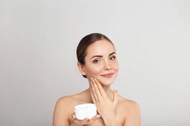Beauty Woman Face Skin Care. Portrait Of Attractive Young Female Applying Cream  And Holding Bottle. Closeup Of Smiling Girl With Natural Makeup And Fresh Skin. Beauty Cosmetics. clipart