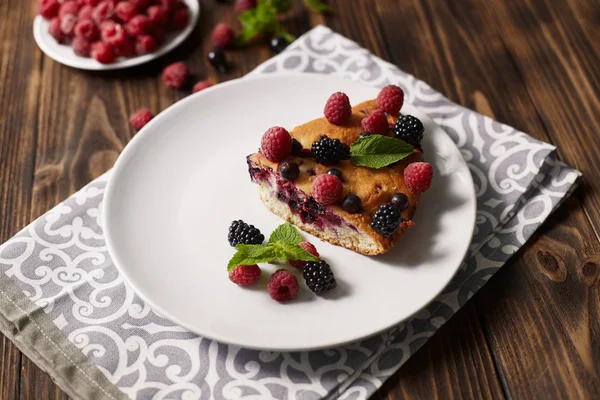 Bir tabakta yaban mersini ile pasta parçası, ahşap bir tahta arka plan üzerinde peçete