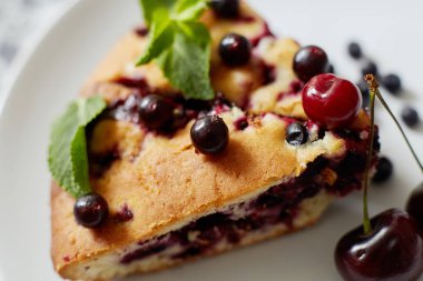 Beyaz bir tabak, peçete üzerinde tatlı için yaban mersini, rasberry, kiraz ve nane ile pasta Parçası. Lezzetli ev yapımı kek parçaları