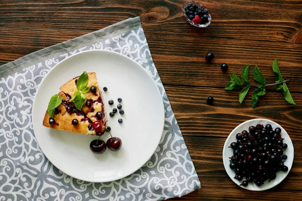 Beyaz bir tabak, peçete tatlı için yaban mersini, rasberry ve nane ile pasta Parçası. Ahşap tahtaarka planda lezzetli ev yapımı kek parçaları