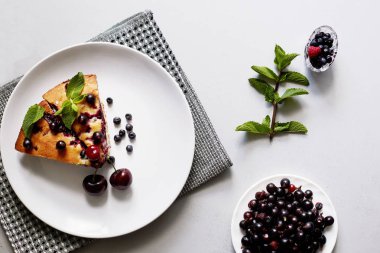 Beyaz bir tabak, peçete üzerinde tatlı için yaban mersini, rasberry, kiraz ve nane ile pasta Parçası. Lezzetli ev yapımı kek parçaları