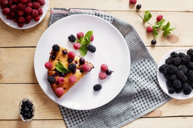 Beyaz bir tabak, peçete tatlı için yaban mersini, rasberry ve nane ile pasta Parçası. Ahşap tahtaarka planda lezzetli ev yapımı kek parçaları