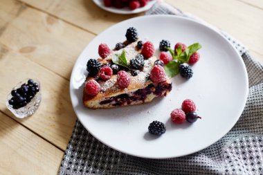 Beyaz bir tabak, peçete tatlı için yaban mersini, rasberry ve nane ile pasta Parçası. Ahşap tahtaarka planda lezzetli ev yapımı kek parçaları