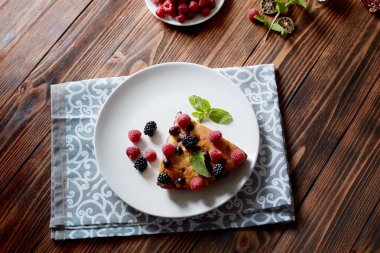 Beyaz bir tabak, peçete tatlı için yaban mersini, rasberry ve nane ile pasta Parçası. Ahşap tahtaarka planda lezzetli ev yapımı kek parçaları