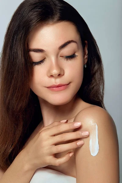 Skin care. Beauty and Spa Concept.  Young pretty woman applying cosmetic cream on her shoulder. Soft skin model with light nude make-up. Skin Protection and dermatology.