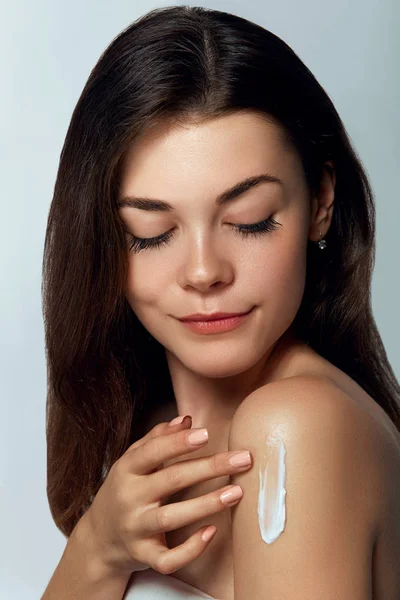 Beauty woman Skin care. Beauty and Spa Concept. Young pretty woman applying cosmetic cream on her shoulder. Soft skin model with light nude make-up. Skin Protection and dermatology.