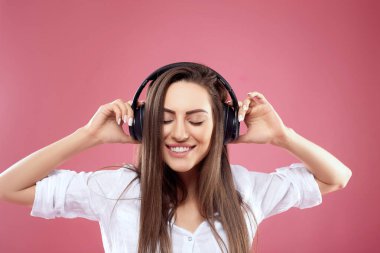 Kablosuz kulaklıklı güzel bir kadın pembe arka planda müzik dinliyor. Kız kablosuz kulaklık kullanıyor.