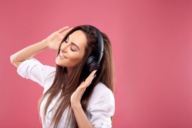Stüdyoda kablosuz kulaklık kullanarak müzik dinleyen güzel bir kadın. Pembe arka planda izole edilmiş. Kablosuz kulaklıklardan ve danstan hoşlanan bir kız..