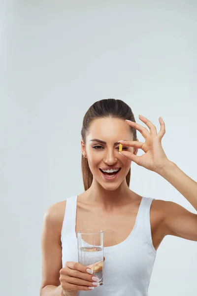 İçeride bir bardak temiz suyla vitamin hapı alan güzel bir kadının portresi. Gülümseyen kız Omega 3 balık yağı kapsülü ve vitamin takviyesi alıyor. Diyet beslenme konsepti