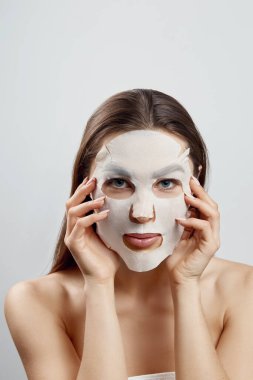 Yüzüne bez nemlendirici maske takmış güzel bir kadın. Yüz ve kaplıca tedavisi. Kozmetik maske.