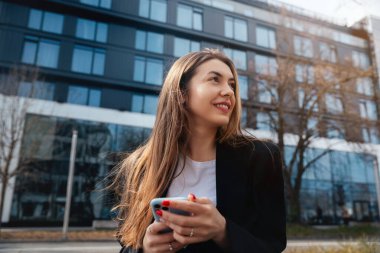 Young woman smiling while holding smartphone outdoors in urban s