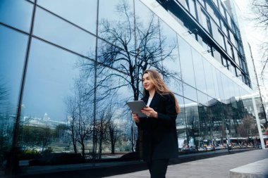 Professional woman walking with tablet near modern glass buildin