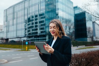 Young woman engaged with a tablet in an urban environment featuring modern buildings, highlighting a contemporary technology lifestyle